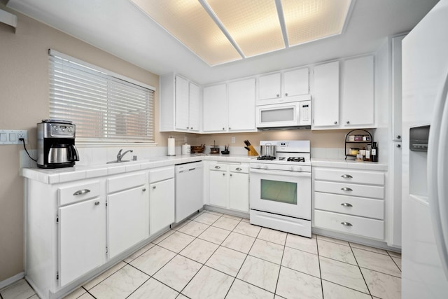 kitchen featuring sink, white appliances, light tile patterned floors, tile counters, and white cabinets