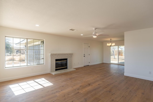 unfurnished living room with a brick fireplace, ceiling fan with notable chandelier, and light hardwood / wood-style flooring