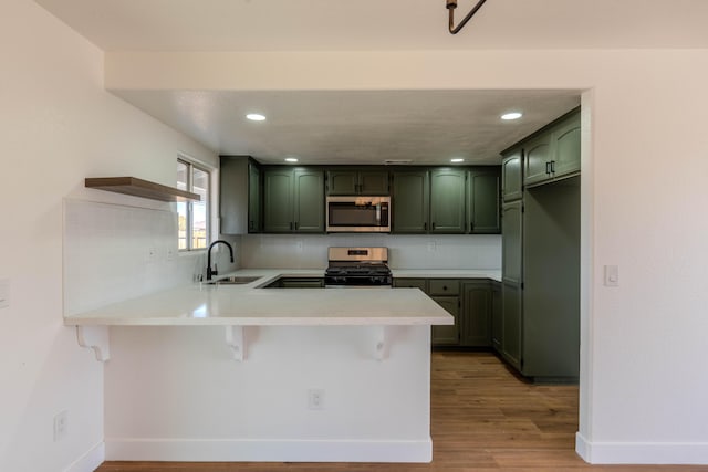 kitchen with a breakfast bar, kitchen peninsula, sink, green cabinetry, and stainless steel appliances