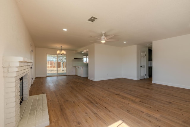 unfurnished living room featuring hardwood / wood-style flooring, ceiling fan with notable chandelier, and a brick fireplace