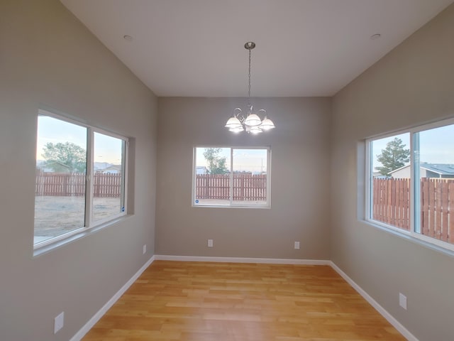 empty room with plenty of natural light, an inviting chandelier, and light hardwood / wood-style flooring