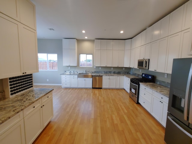 kitchen featuring appliances with stainless steel finishes, sink, white cabinets, light stone counters, and light hardwood / wood-style floors