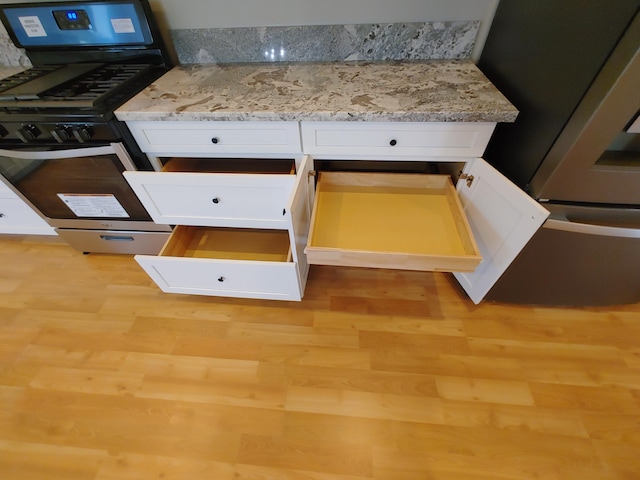 details featuring light stone countertops, range with gas stovetop, light hardwood / wood-style floors, and white cabinets