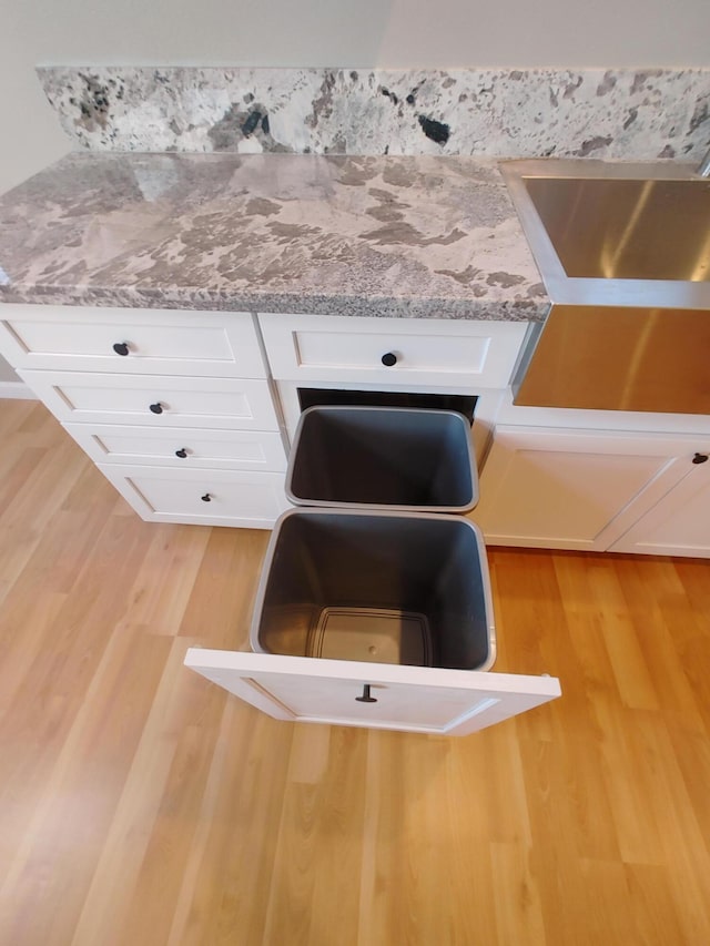 room details with white cabinetry, light stone countertops, and light wood-type flooring