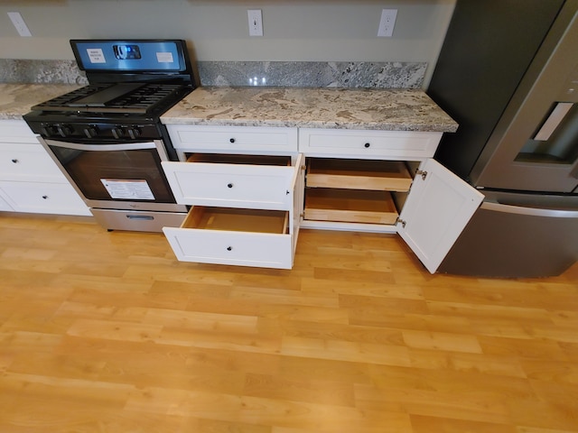 kitchen with stainless steel appliances, light stone countertops, light wood-type flooring, and white cabinets