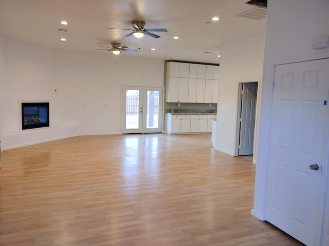 unfurnished living room with a high ceiling, ceiling fan, and light hardwood / wood-style floors