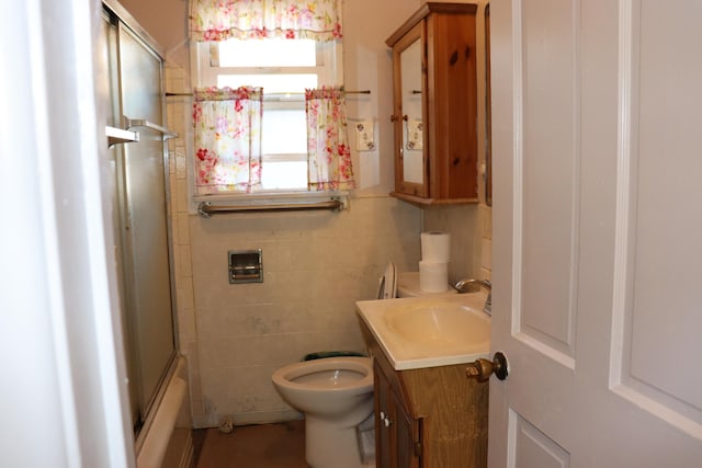 full bathroom with vanity, combined bath / shower with glass door, tile walls, and toilet