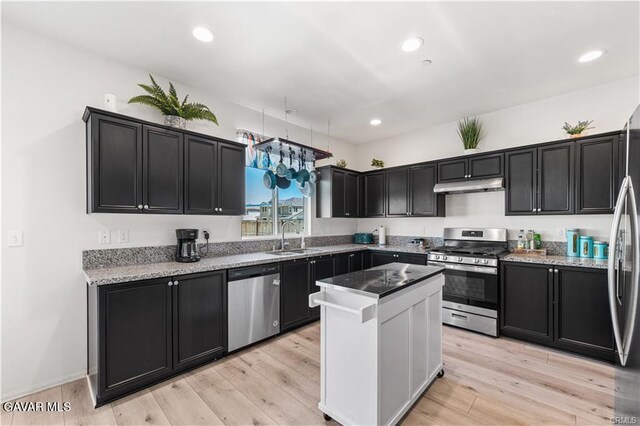 2436 Lugar Bonito Ct, Rosamond, CA 93560 - kitchen featuring stainless steel appliances, under cabinet range hood, dark cabinetry, a center island, and light stone counters