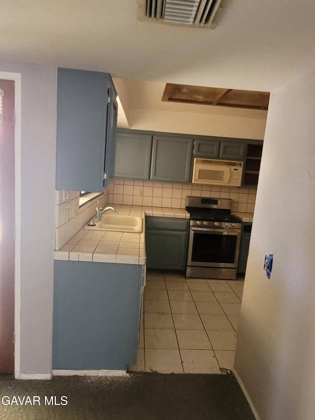 964 Roosevelt St, Ridgecrest, CA 93555 - kitchen with stainless steel gas range oven, white microwave, tile countertops, backsplash, and gray cabinetry