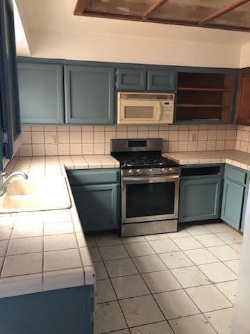 964 Roosevelt St, Ridgecrest, CA 93555 - kitchen featuring gas range, white microwave, tile counters, open shelves, and decorative backsplash