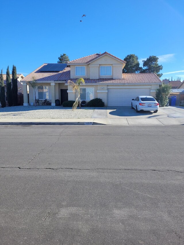 view of front of house with driveway, a garage, roof mounted solar panels, and a tiled roof