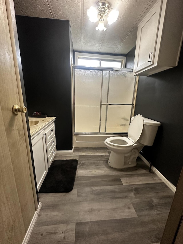 full bathroom featuring hardwood / wood-style floors, bath / shower combo with glass door, a textured ceiling, toilet, and vanity