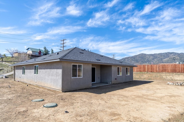 rear view of house with fence, a mountain view, roof with shingles, and stucco siding