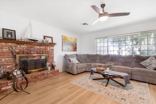 living room with ceiling fan, a brick fireplace, a healthy amount of sunlight, and light hardwood / wood-style floors