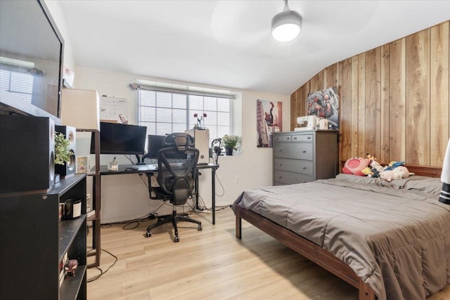 bedroom with lofted ceiling, light wood-type flooring, and wooden walls