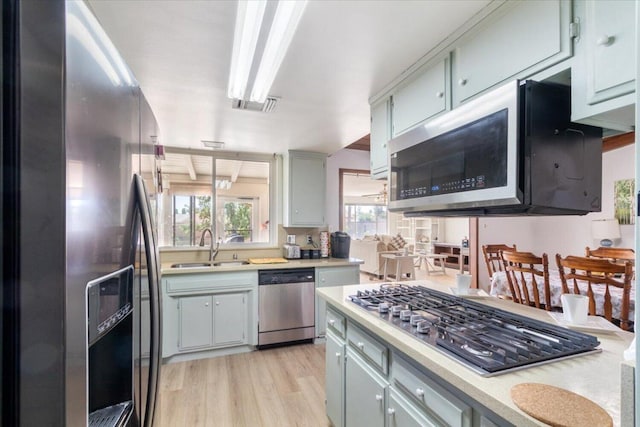 kitchen with appliances with stainless steel finishes, decorative light fixtures, light hardwood / wood-style floors, and sink