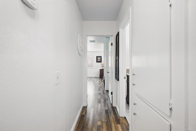 corridor featuring baseboards and dark wood-type flooring