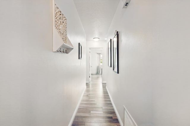hall featuring baseboards, a textured ceiling, wood finished floors, and visible vents