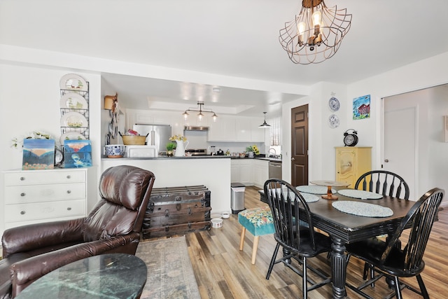 dining space featuring light wood-style floors, a raised ceiling, and a chandelier