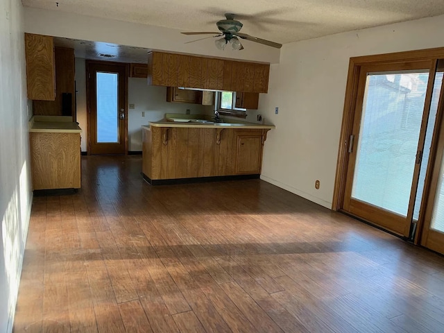 kitchen with a peninsula, dark wood finished floors, a ceiling fan, light countertops, and a sink