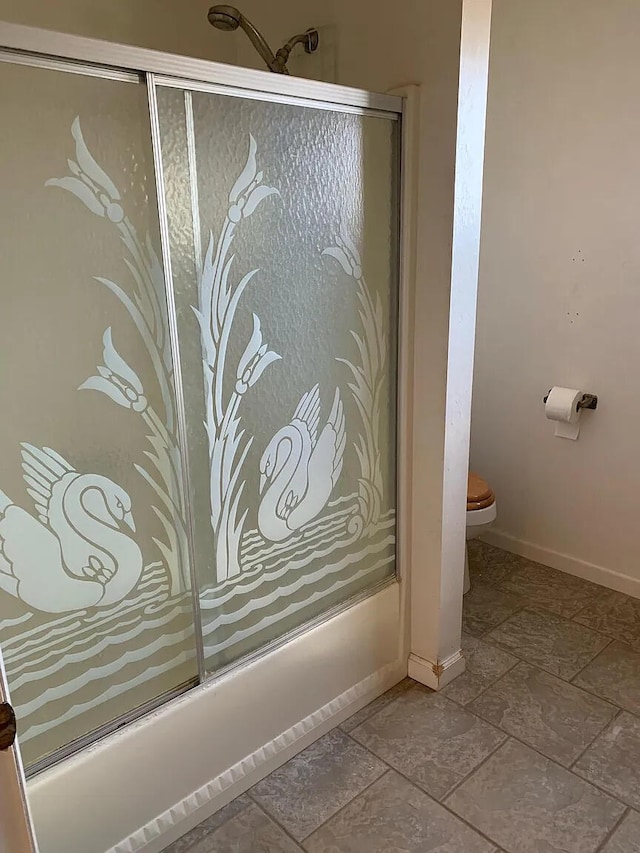full bath featuring combined bath / shower with glass door, toilet, baseboards, and stone finish flooring