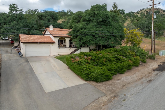 mediterranean / spanish-style home featuring a chimney, a tile roof, stucco siding, driveway, and a garage