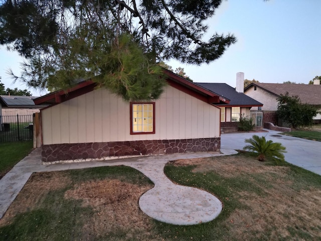 view of side of home featuring concrete driveway, fence, a chimney, and a lawn