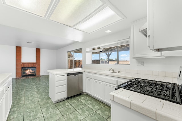 kitchen with a peninsula, a sink, white cabinetry, open floor plan, and tile counters