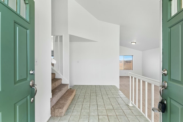 foyer with lofted ceiling, light tile patterned floors, stairs, and light carpet