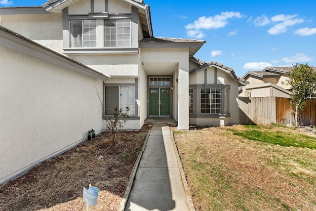 doorway to property with a yard, fence, and stucco siding