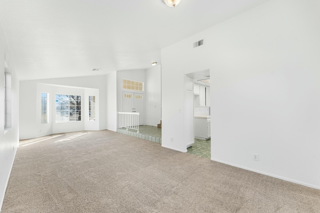 unfurnished living room with lofted ceiling, baseboards, visible vents, and light colored carpet