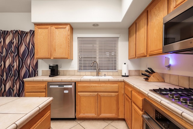 kitchen with tile countertops, light tile patterned floors, sink, and appliances with stainless steel finishes