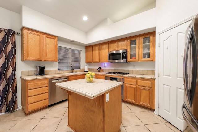 kitchen with appliances with stainless steel finishes, a center island, light tile patterned floors, and tile counters