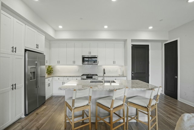 kitchen featuring sink, white cabinets, dark hardwood / wood-style flooring, stainless steel appliances, and a center island with sink