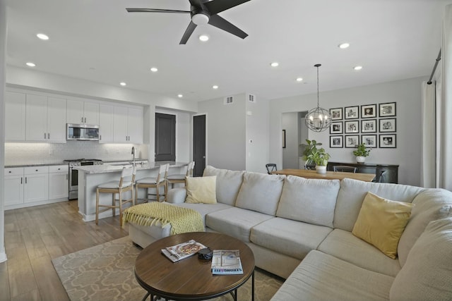 living room featuring ceiling fan with notable chandelier and light hardwood / wood-style floors