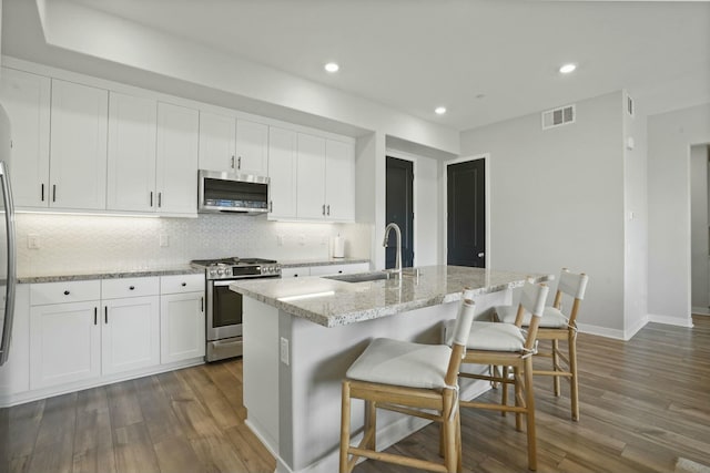 kitchen featuring appliances with stainless steel finishes, sink, a kitchen breakfast bar, a kitchen island with sink, and light stone countertops