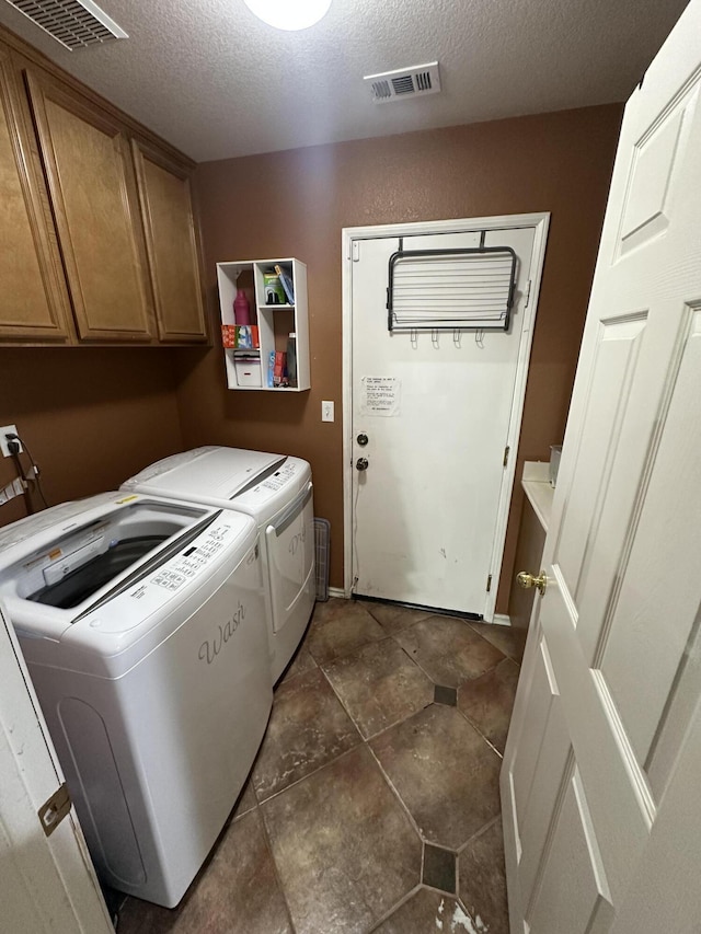 laundry area with washing machine and clothes dryer, cabinets, and a textured ceiling