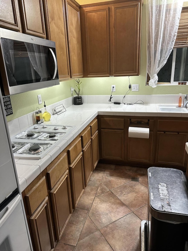 kitchen featuring white gas cooktop, refrigerator, sink, dark tile patterned floors, and tile counters