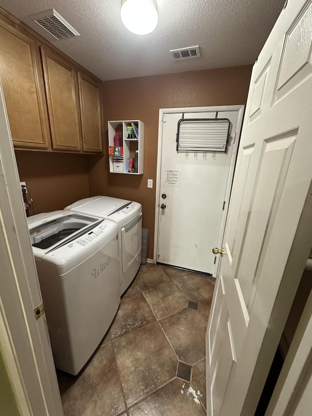 laundry area with washer and dryer, a textured ceiling, and cabinets