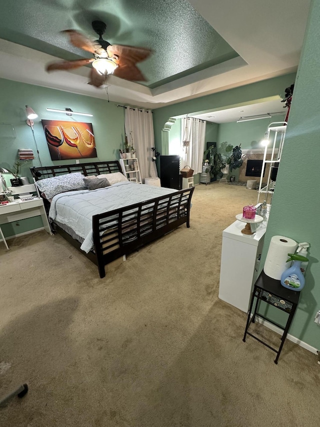 bedroom with ceiling fan, a raised ceiling, carpet floors, and a textured ceiling