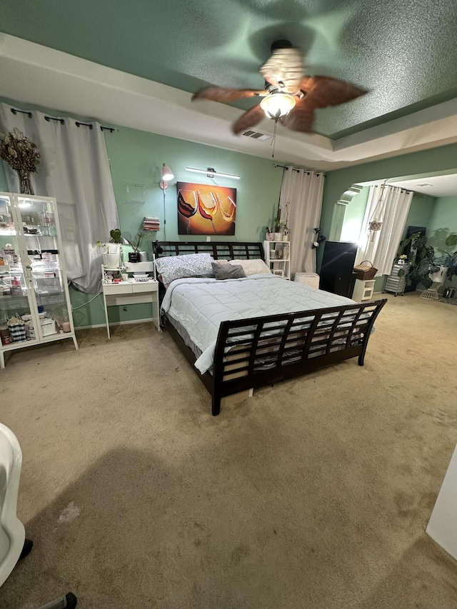 carpeted bedroom with a tray ceiling, ceiling fan, and a textured ceiling