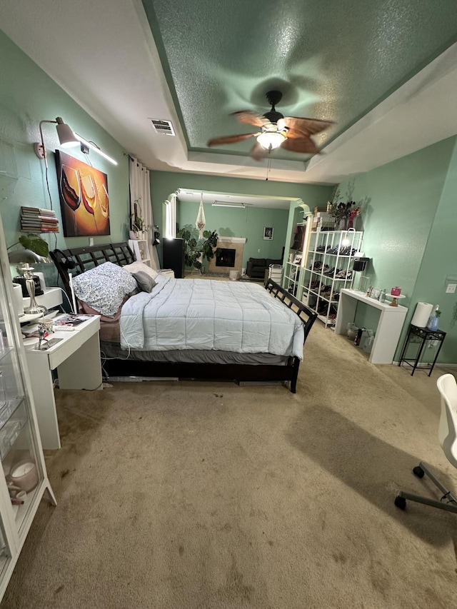 bedroom featuring carpet, ceiling fan, a textured ceiling, and a tray ceiling