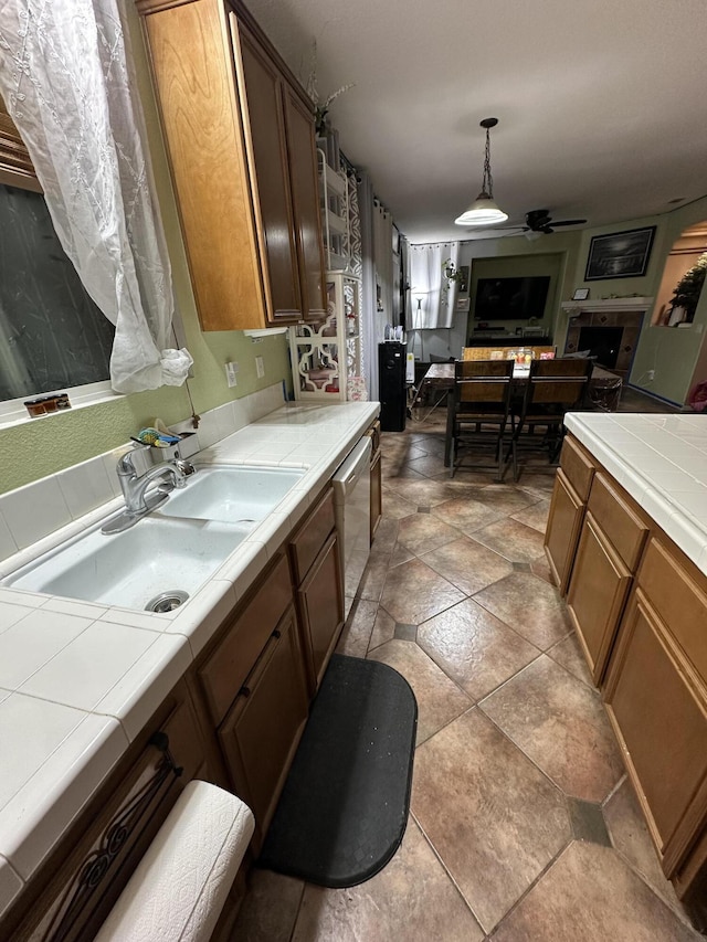 kitchen featuring tile countertops, pendant lighting, sink, stainless steel dishwasher, and ceiling fan