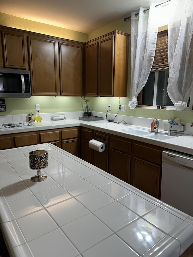 kitchen with tile counters, white appliances, and sink