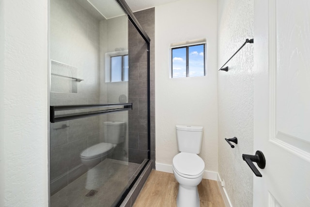 bathroom featuring hardwood / wood-style floors, a shower with shower door, and toilet