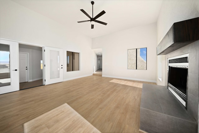 unfurnished living room with ceiling fan, french doors, a towering ceiling, and light hardwood / wood-style floors