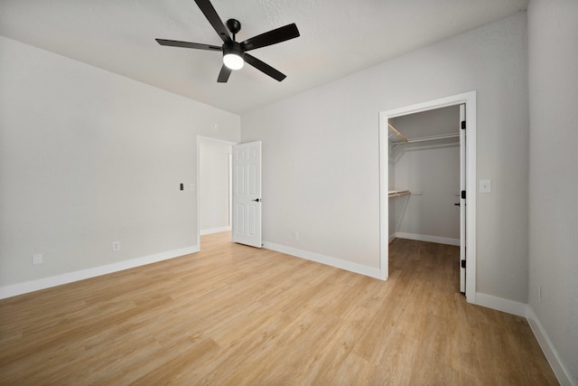 unfurnished bedroom featuring a spacious closet, a closet, ceiling fan, and light hardwood / wood-style floors