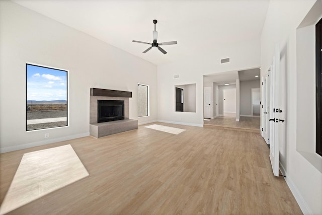 unfurnished living room featuring ceiling fan, light wood-type flooring, a high ceiling, and a tiled fireplace