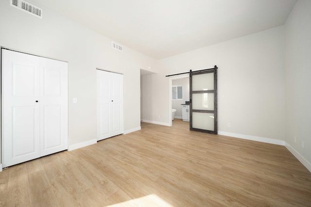 unfurnished bedroom featuring a barn door, light hardwood / wood-style floors, ensuite bath, and multiple closets