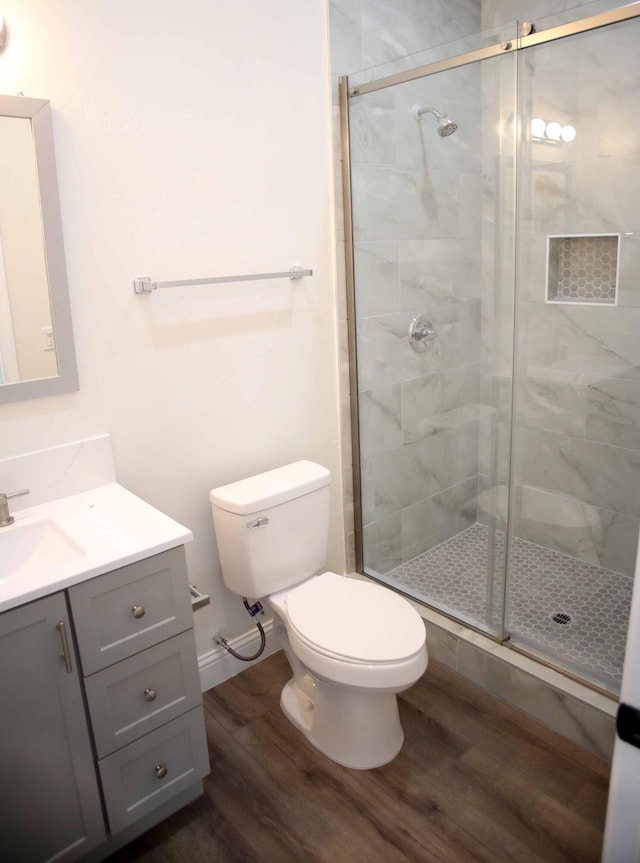 bathroom with vanity, toilet, wood finished floors, and a stall shower
